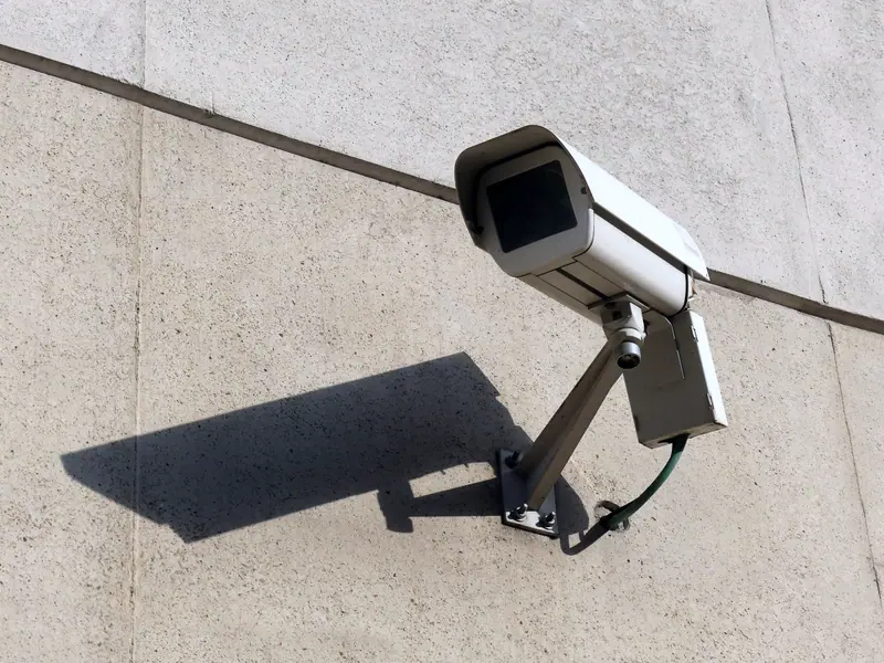 Surveillance camera on a concrete wall casting a long shadow